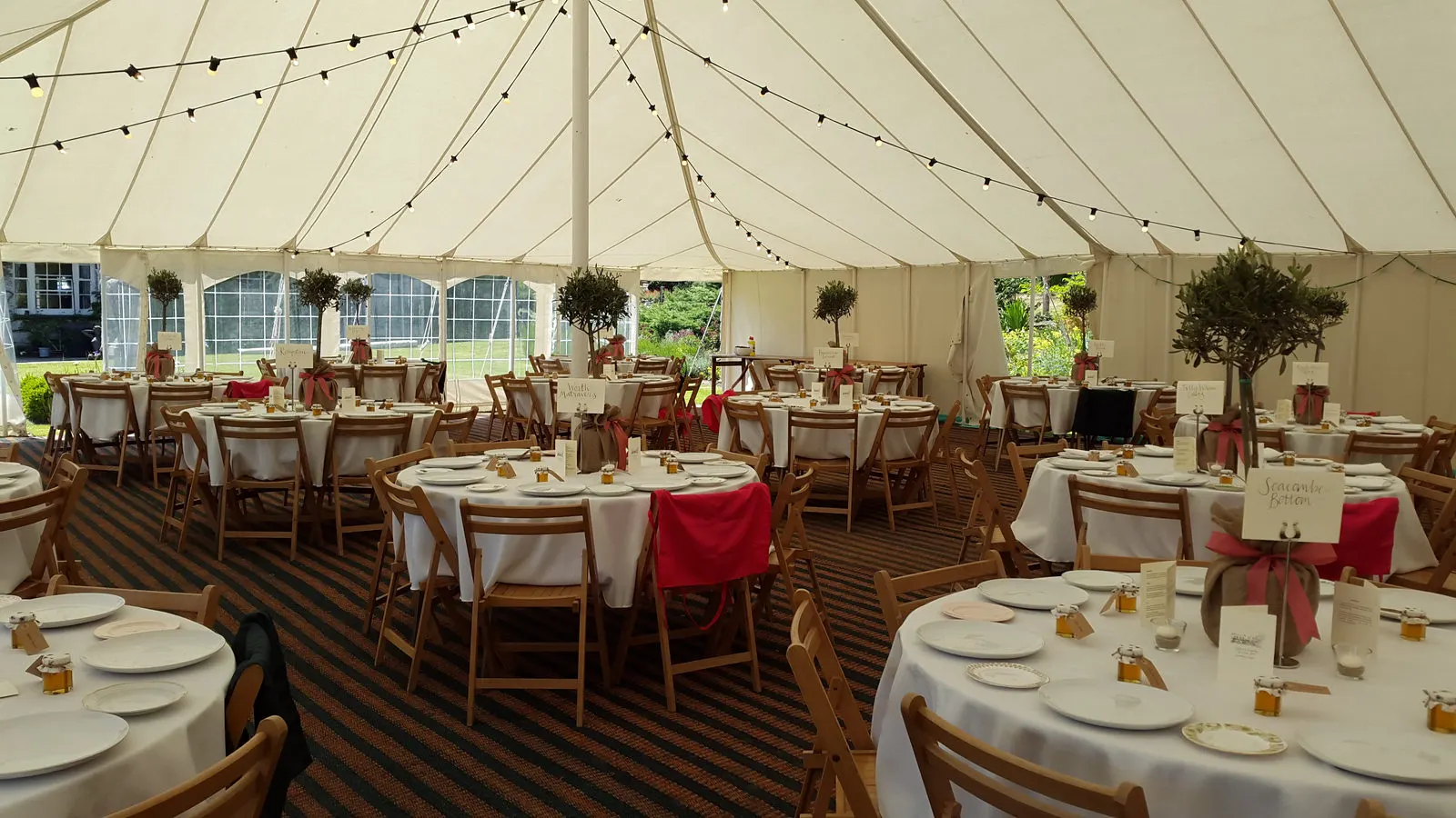 Marquee interior with festoon lights, round tables and wooden chairs
