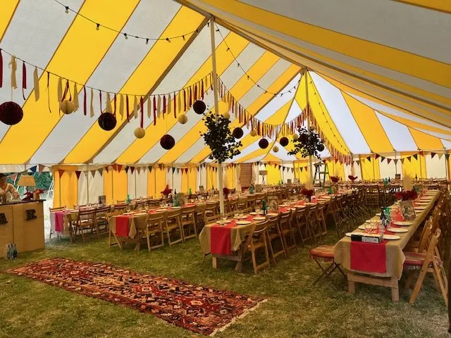 Long dressed tables under bunting inside a yellow and white striped marquee