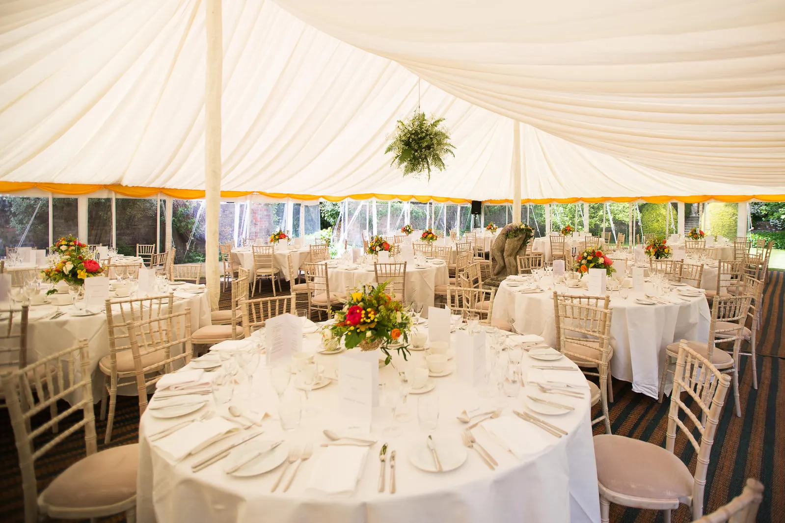 Round tables laid with white linen, glassware and flowers inside a lined marquee